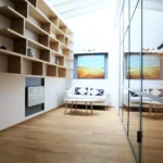 Espace détente sous verrière de toit, avec bibliothèque intégrée, canapé blanc, lumière naturelle abondante et parquet bois clair.