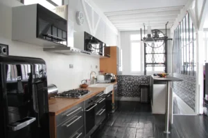 Cuisine de loft au design industriel avec électroménager SMEG, crédence en carrelage noir et blanc, verrière atelier et parquet sombre, située à Paris 10ᵉ.