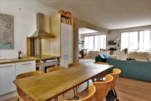 Cuisine ouverte sur le séjour avec hotte en inox, table en bois massif et chaises en rotin dans un loft lumineux situé rue de Chabrol à Paris 10ᵉ.