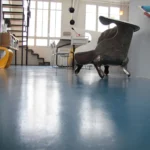 Fauteuil design en métal et velours dans un loft lumineux du 10e arrondissement de Paris, avec sol bleu, escalier graphique et grandes fenêtres style atelier.