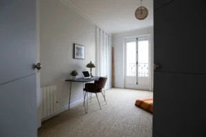 Chambre lumineuse avec coin bureau, grande fenêtre et sol en fibre naturelle – appartement à vendre à Belleville, Paris 19ᵉ.