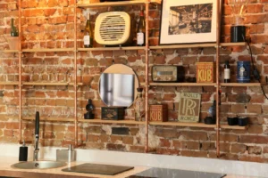 Détail d’un mur en briques décoré d’étagères cuivrées, objets rétro et verrerie dans la cuisine d’un appartement à vendre à Montmartre Paris 18.