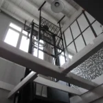 Structure de monte-charge d’atelier dans un loft industriel parisien, avec charpente apparente peinte en blanc et verrière donnant sur la cuisine, Paris 10ᵉ.