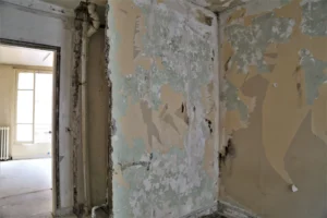 Mur endommagé avec anciennes peintures à décoller, dans l’appartement attenant au local commercial.