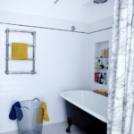 Salle de bain avec baignoire sur pieds et douche pluie, murs en faïence blanche et détails rétro dans un loft à vendre à Paris 10ᵉ, secteur Faubourg Saint-Denis.