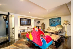 Salon cosy et original d’un loft à Paris 17 – Canapés aux formes atypiques, tableau de chevaux bleus, télé murale et objets de décoration artistiques.