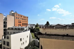 Vue dégagée depuis le loft sur les toits de Paris 10ᵉ, avec aperçu du marché Saint-Quentin et ciel bleu en arrière-plan.