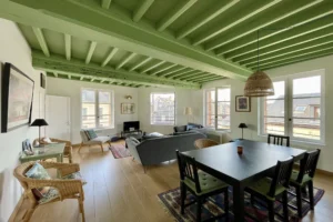 Vue générale du séjour avec plafond à poutres vertes, espace salon et salle à manger lumineux dans un appartement à vendre à Honfleur Quality Street Immobilier.