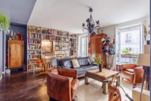 Salon lumineux avec bibliothèque murale et grandes fenêtres dans un appartement à vendre Paris 18 Montmartre, proche du Théâtre de l’Atelier