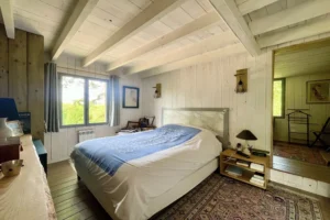 Chambre principale avec lit double, murs en bois clair et vue verdoyante