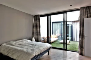 Chambre parentale avec parquet et large baie vitrée donnant sur un patio verdoyant, dans un loft à Nanterre.