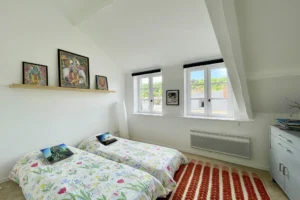 Chambre d’enfants sous combles avec deux lits simples et fenêtres en enfilade, dans un appartement lumineux à vendre à Honfleur.
