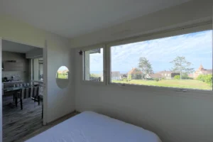 Chambre lumineuse avec vue panoramique sur la mer et ouverture sur la cuisine dans un appartement à Benerville-sur-Mer.