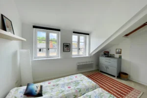 Chambre sous combles avec deux fenêtres et rangements, dans un appartement à vendre à Honfleur, idéal pour enfants ou invités.