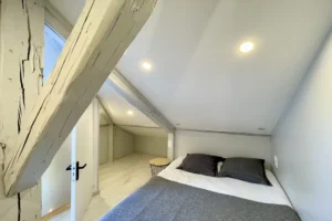 Chambre mansardée avec lit double, poutres apparentes et parquet clair dans un appartement duplex à Deauville.