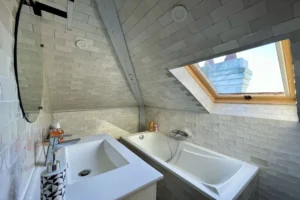 Salle de bains mansardée avec baignoire, vasque moderne et fenêtre de toit dans un appartement duplex à Deauville.
