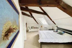 Chambre parentale spacieuse sous combles avec poutres apparentes et coin détente, dans un appartement à vendre à Honfleur.