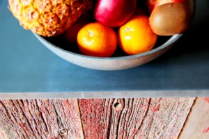 Gros plan sur une corbeille de fruits posée sur un plan de travail en béton et bois brut, dans un appartement à Belleville – Paris 19ᵉ.