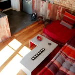 Vue plongeante sur un salon avec mur en briques apparentes, canapé modulaire rouge et sol en parquet, dans un appartement à Belleville – Paris 19ᵉ.