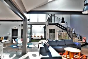Salon baigné de lumière naturelle dans un loft à Nanterre, avec verrière, grande hauteur sous plafond et escalier métallique design.