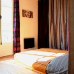 Chambre avec lit double au sol, lumière naturelle et rideaux épais, dans un appartement chaleureux à Belleville.