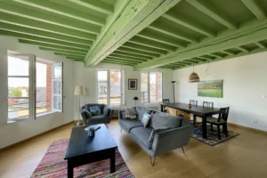 Vue d’angle du séjour dans un appartement lumineux à vendre à Honfleur, avec plafond en bois peint et espace salle à manger.