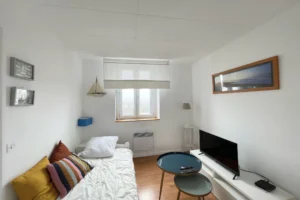 Petit salon TV aménagé avec banquette, tables gigognes et fenêtre sur la ville.