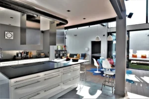 Cuisine équipée avec îlot central et hotte suspendue dans un loft à Nanterre, ouverte sur salle à manger et patio extérieur.