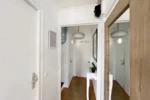 Couloir d’entrée avec console blanche, miroir et suspension, menant à la pièce de vie.