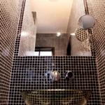 Salle d’eau avec vasque en verre et murs en carrelage noir à petits carreaux dans un style contemporain.