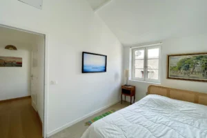 Chambre lumineuse avec lit double et fenêtre donnant sur les toits d’Honfleur, dans un appartement à vendre dans le Calvados.