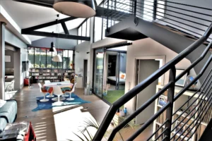 Vue depuis l’escalier sur la salle à manger du loft à Nanterre, avec verrière, parquet en bois clair et accès à la chambre sur patio.