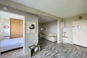 Entrée de l’appartement avec vue sur le salon et la chambre, sol effet bois vieilli et ambiance douce à Benerville-sur-Mer.