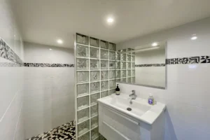 Salle d’eau contemporaine de l’appartement en duplex à vendre à Deauville, avec paroi en briques de verre et carrelage décoratif.