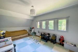 Chambre d’enfant lumineuse située à l’étage, avec lit simple, espace de jeux et fenêtres donnant sur la verdure à Ouilly-le-Vicomte.