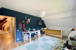 Chambre d’enfant à l’étage avec mur bleu nuit, coin bureau, parquet bois et lit simple à Ouilly-le-Vicomte.