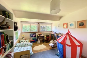Chambre d’enfant aux couleurs ludiques avec lit, bibliothèque, coin jeux et vue sur jardin à Ouilly-le-Vicomte.