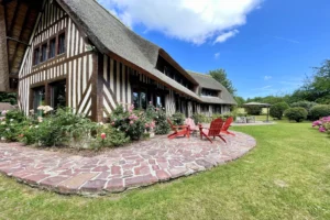 Vue extérieure d’une maison normande à Ouilly-le-Vicomte avec façade à colombages, terrasse en pierre et jardin paysager.