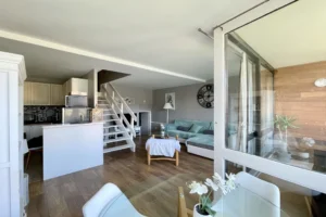 Pièce de vie de l’appartement en duplex à vendre à Deauville, comprenant le salon, la cuisine ouverte et l’escalier menant à l’étage.