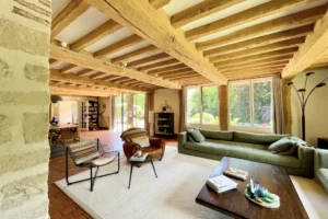 Salon spacieux baigné de lumière naturelle, avec poutres apparentes, grandes fenêtres et mobilier contemporain à Ouilly-le-Vicomte.