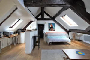 Vue principale de l’appartement sous combles à Paris 3ᵉ, rue de Turenne – espace lumineux avec poutres apparentes, coin cuisine et salon sous les toits.