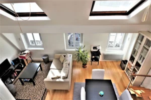 Vue du séjour lumineux du loft à vendre à Paris 9, quartier Martyrs – Notre-Dame-de-Lorette, avec grandes fenêtres, parquet bois et coin salon contemporain.