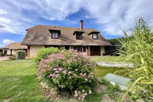 Façade principale de la maison à vendre à Moisville dans l’Eure, avec jardin paysager, bassin et fleurs en premier plan