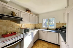 Cuisine aménagée avec mobilier traditionnel et fenêtre sur jardin dans une maison normande à Bonneville-la-Louvet.