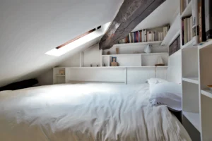 Chambre en mezzanine sous combles avec rangements et bibliothèque intégrée, poutre apparente et fenêtre de toit, appartement rue de Turenne Paris 3ᵉ.