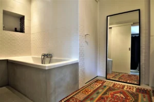 Salle de bain du loft à Paris 11 Parmentier avec baignoire moderne, carrelage blanc texturé et grand miroir.