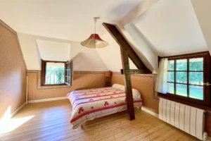 Chambre à l’étage avec poutre apparente et fenêtres sur jardin dans une maison normande à Bonneville-la-Louvet.