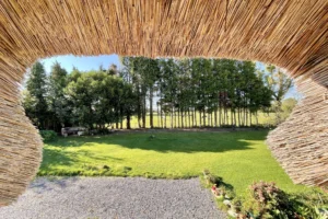 Vue sur le jardin depuis l’étage sous le toit de chaume d’une maison normande à Bonneville-la-Louvet.