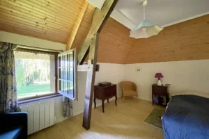 Chambre à l’étage avec poutres apparentes et fenêtre donnant sur le jardin dans une maison normande à Bonneville-la-Louvet.
