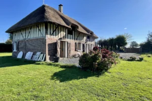 Maison normande à Bonneville-la-Louvet (Calvados) avec façade en colombages, jardin fleuri et toit de chaume traditionnel.